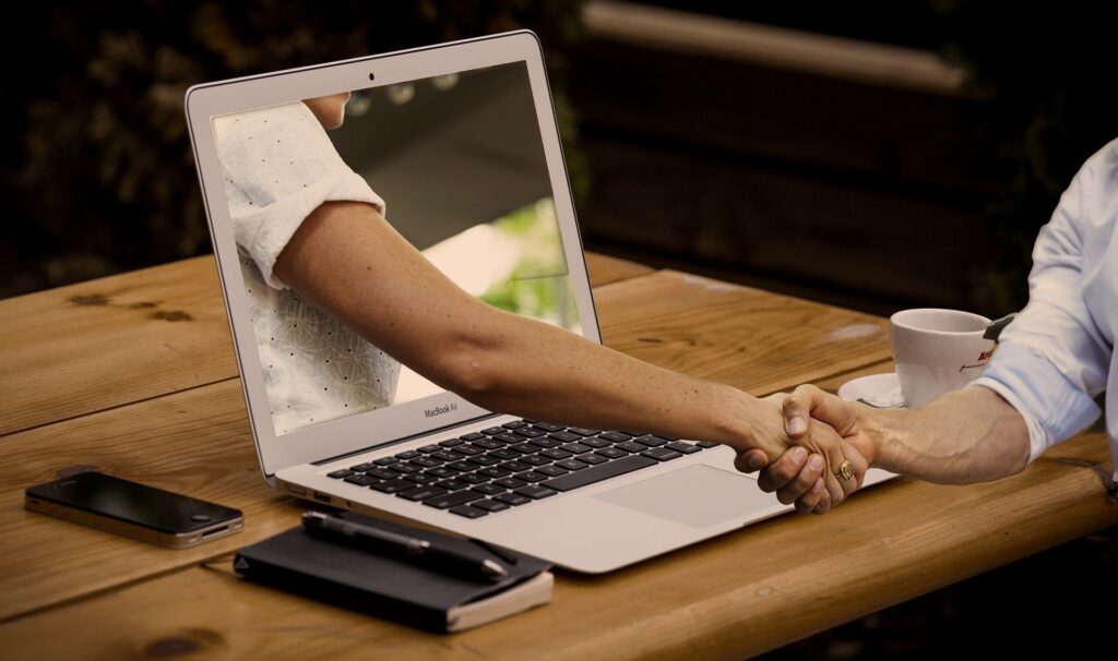 Dos manos estrechándose a través de un laptop.